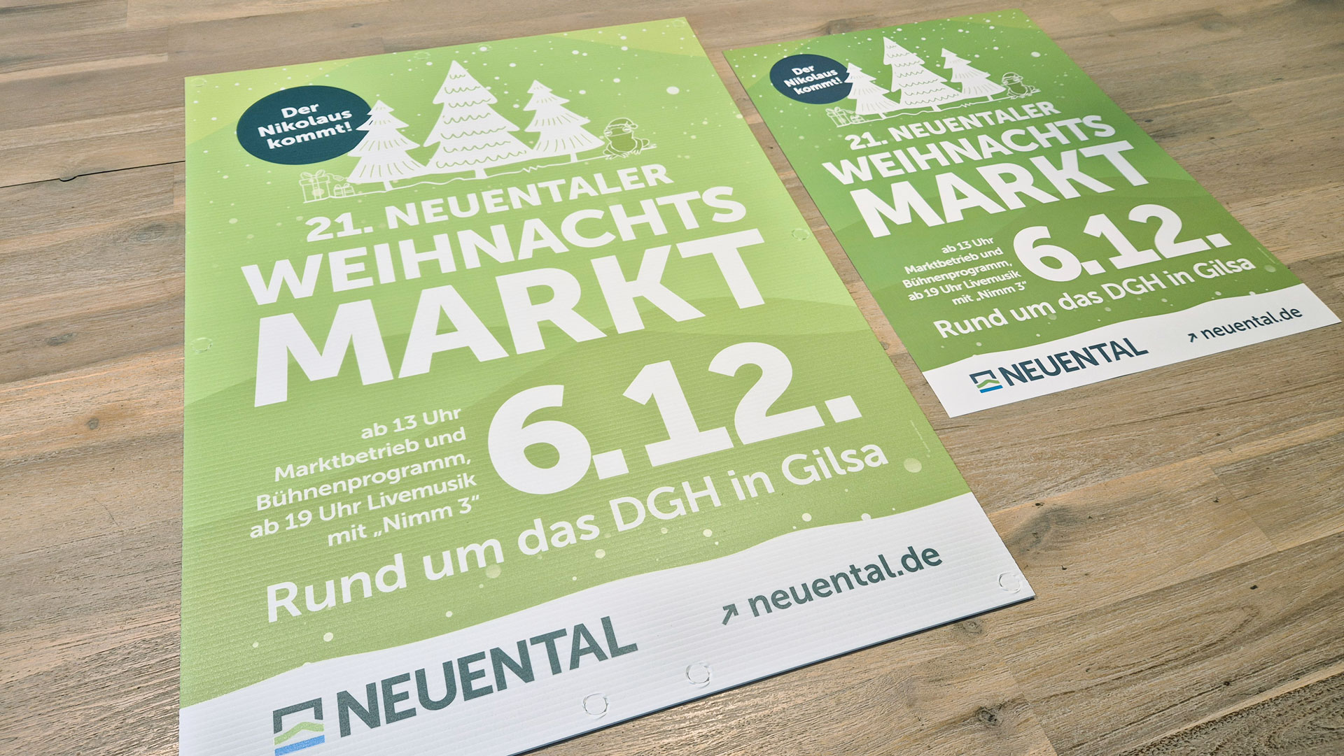Zwei Plakate zum Weihnachtsmarkt der Gemeinde Neuental in verschiedenen Größen liegen auf einem Holztisch