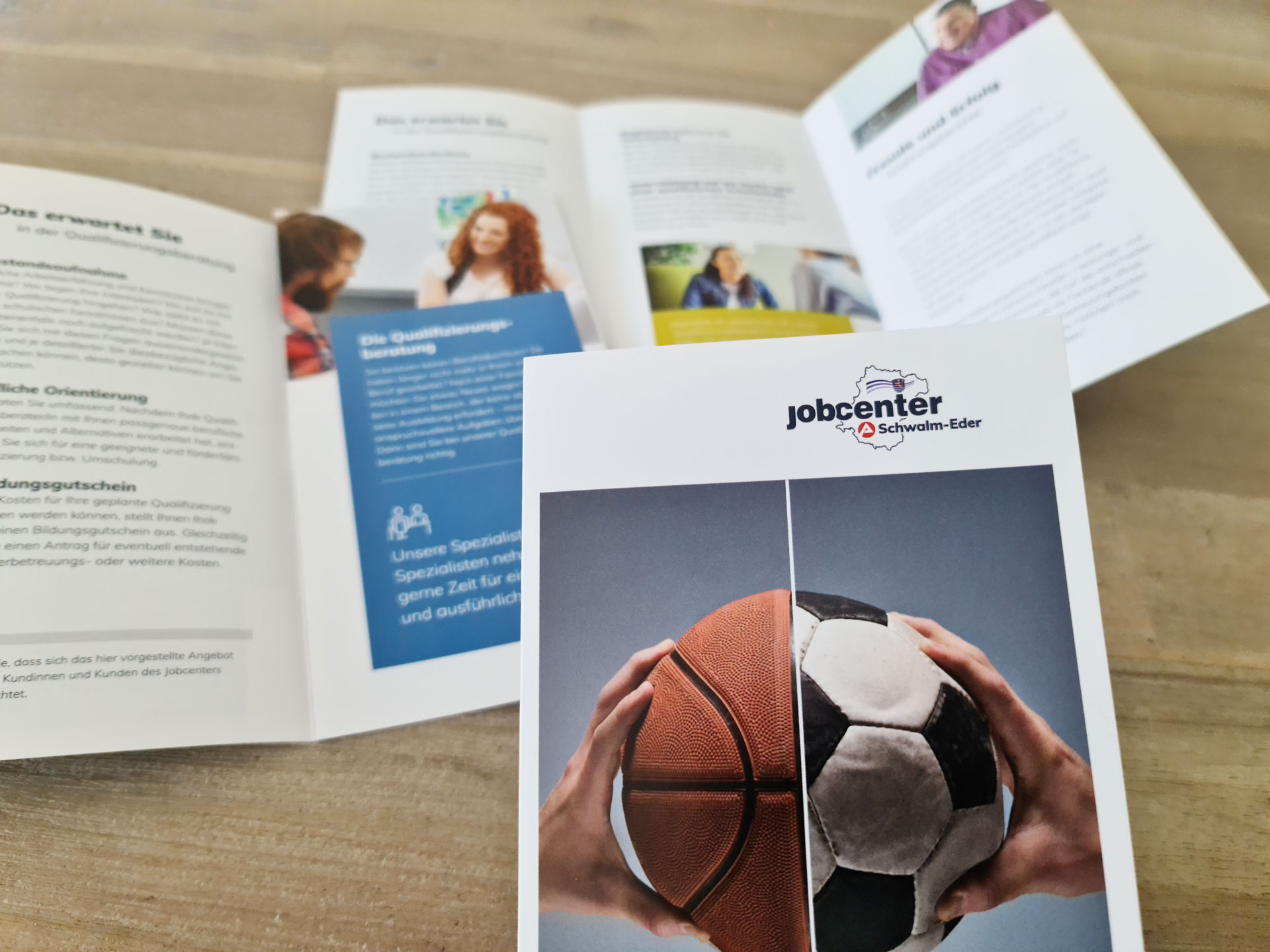 Auf einem Holztisch liegen zu- und aufgeklappte Folder des Jobcenters Schwalm-Eder
