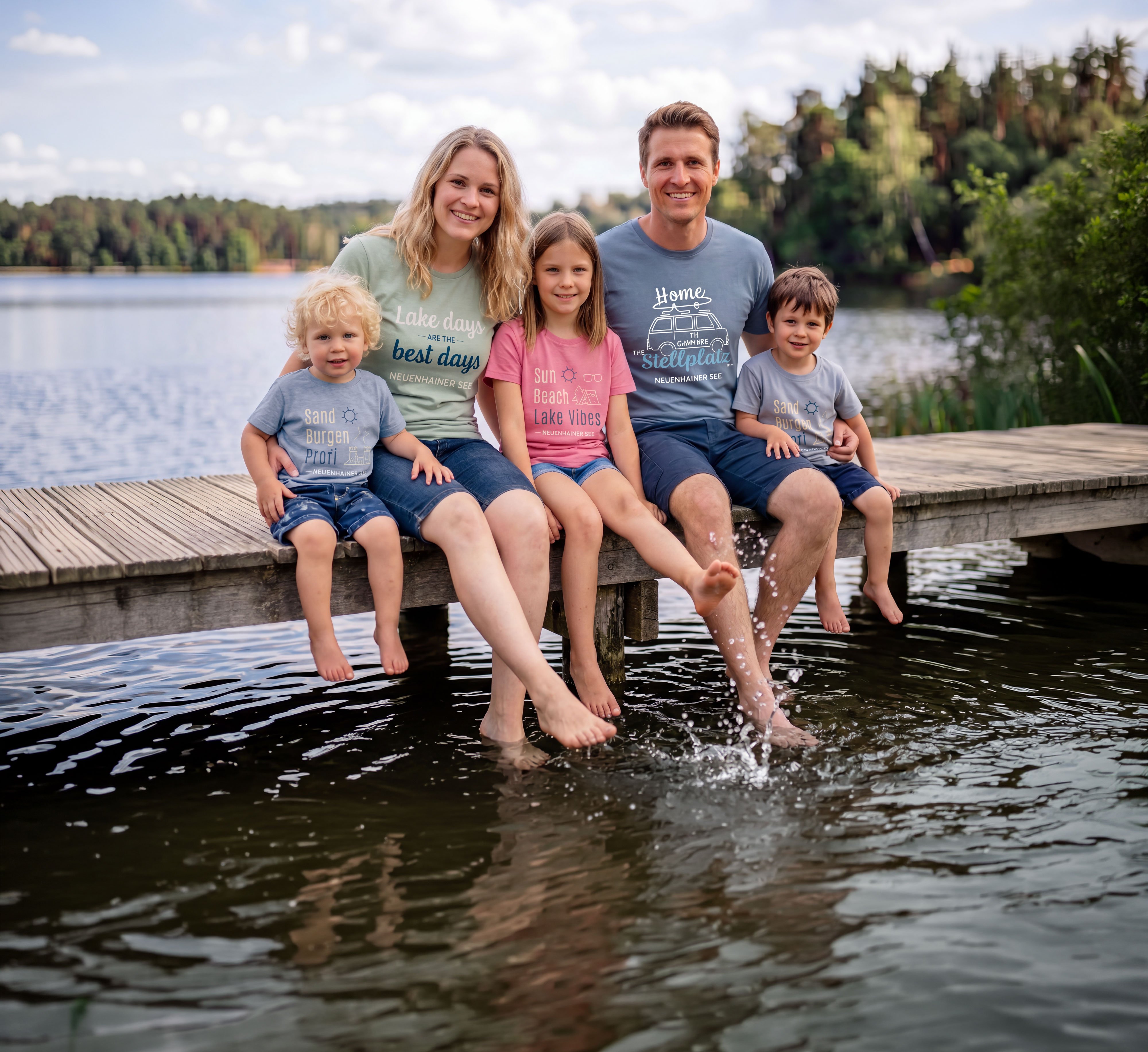 Familie sitzt auf einem Steg am Wasser und lacht in die Kamera